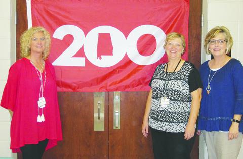 Lynn Principal Jennifer Baker; Cynthia Tittle, second and third grade math and second grade science teacher and Lisa Cagle, reading coach specialist pose in front of the Alabama 200 flag.