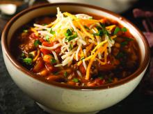 A photo of a bowl of chili topped with cheese and scallions.